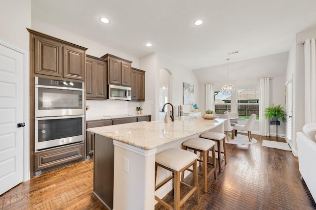 3234 Burke Dr, Royse City, TX 75189 - kitchen with appliances with stainless steel finishes, a breakfast bar area, dark wood-type flooring, light stone countertops, and an island with sink