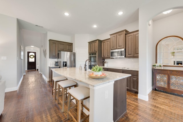 3234 Burke Dr, Royse City, TX 75189 - kitchen with stainless steel appliances, arched walkways, a breakfast bar area, light stone counters, and dark wood-type flooring