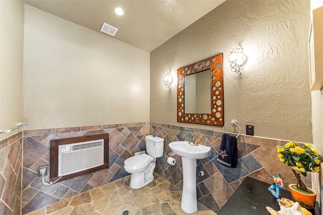 1621 Grandberry Dr, Melissa, TX 75454 - bathroom with toilet, stone finish floors, a sink, a textured wall, and tile walls