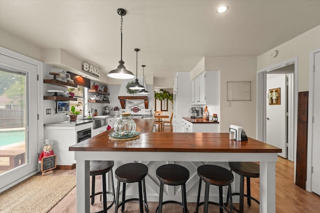 2302 Warwick Ave, Grand Prairie, TX 75052 - kitchen with white cabinets, light wood-type flooring, open shelves, pendant lighting, and a breakfast bar area
