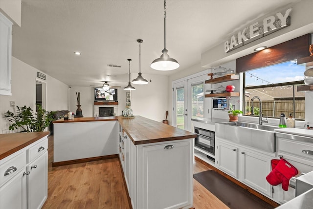 2302 Warwick Ave, Grand Prairie, TX 75052 - kitchen featuring wooden counters, a sink, a fireplace, white cabinetry, and light wood-style flooring