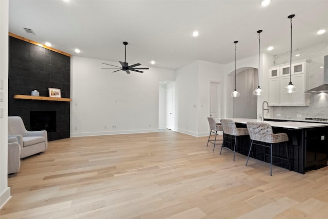 1812 Welker Dr, Van Alstyne, TX 75495 - kitchen featuring light wood finished floors, a breakfast bar area, light countertops, wall chimney range hood, and a kitchen island with sink