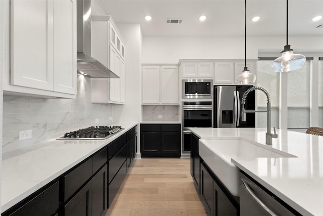 1812 Welker Dr, Van Alstyne, TX 75495 - kitchen featuring wall chimney exhaust hood, stainless steel appliances, white cabinets, dark cabinetry, and light wood-style floors