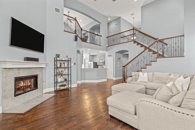 2433 Mallard Dr, Little Elm, TX 75068 - living area with arched walkways, wood finished floors, a towering ceiling, a tiled fireplace, and stairs