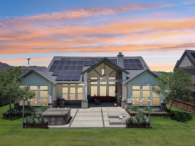 424 Trigger Trl, Argyle, TX 76226 - back of property at dusk featuring board and batten siding, a hot tub, a patio area, roof mounted solar panels, and a chimney