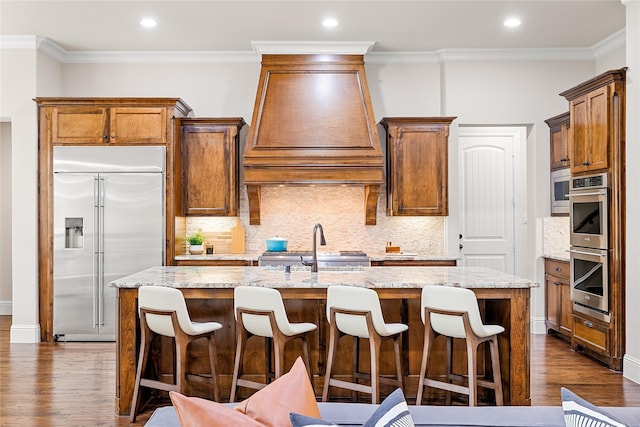 655 Creekway Dr, Irving, TX 75039 - kitchen with appliances with stainless steel finishes, custom range hood, dark wood-style floors, a kitchen island with sink, and ornamental molding