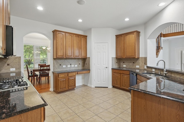 2410 Honey Dr, Arlington, TX 76001 - kitchen with arched walkways, stainless steel appliances, dark stone counters, backsplash, and brown cabinets