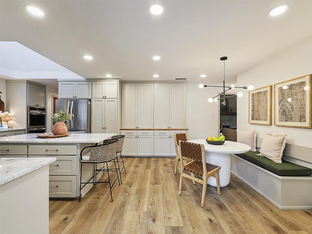 6512 Elkhurst Dr, Plano, TX 75023 - kitchen with stainless steel appliances, light wood-type flooring, a kitchen breakfast bar, light stone counters, and recessed lighting