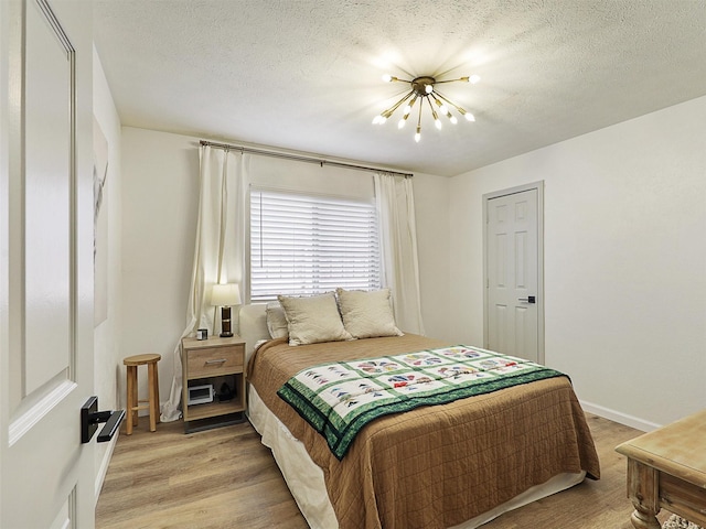 6512 Elkhurst Dr, Plano, TX 75023 - bedroom with a chandelier, light wood-style floors, baseboards, and a textured ceiling