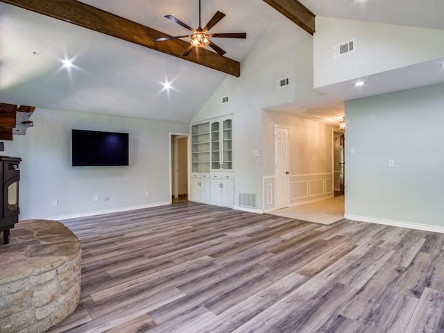 7710 Ravenswood Rd, Granbury, TX 76049 - unfurnished living room with beamed ceiling, a wood stove, wood finished floors, a ceiling fan, and high vaulted ceiling
