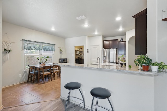 7113 Creighton Ct, Fort Worth, TX 76120 - kitchen featuring stainless steel fridge with ice dispenser, dark brown cabinets, a breakfast bar area, a peninsula, and light stone countertops