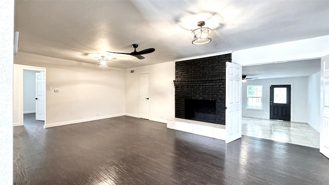 3315 Cedarcroft Ln, Dallas, TX 75233 - unfurnished living room with a ceiling fan, wood finished floors, a brick fireplace, baseboards, and a textured ceiling