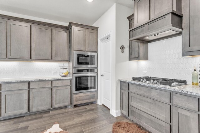 4444 Blue Mist Dr, Fort Worth, TX 76036 - kitchen featuring appliances with stainless steel finishes, backsplash, wood finished floors, and light stone counters