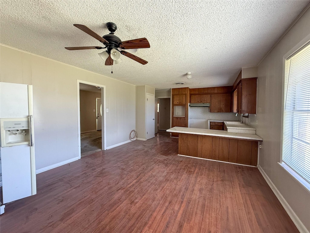1503 4th St, Roscoe, TX 79545 - kitchen with a peninsula, white fridge with ice dispenser, brown cabinets, dark wood-style floors, and a textured ceiling
