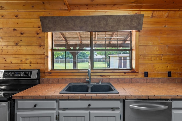 201 Cemetery Rd, Boyd, TX 76023 - kitchen with electric range, stainless steel dishwasher, tile countertops, wooden walls, and white cabinetry