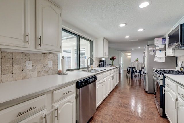 3510 Knoll Point Dr, Garland, TX 75043 - kitchen featuring appliances with stainless steel finishes, a sink, backsplash, wood finished floors, and a textured ceiling