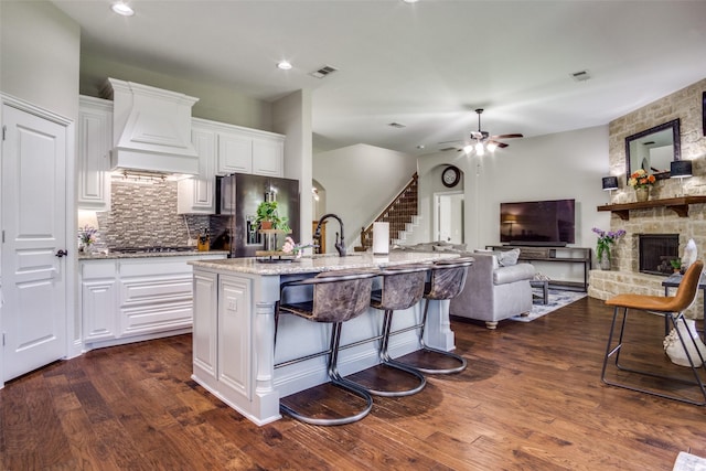 921 Yarwood Way, Burleson, TX 76028 - kitchen featuring premium range hood, refrigerator with ice dispenser, decorative backsplash, light stone countertops, and a center island with sink