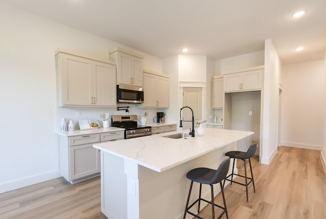 2836 Ave L, Fort Worth, TX 76105 - kitchen featuring a sink, stainless steel appliances, baseboards, a kitchen bar, and light wood finished floors