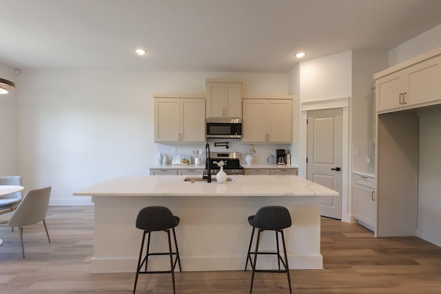2836 Ave L, Fort Worth, TX 76105 - kitchen featuring appliances with stainless steel finishes, a sink, a kitchen bar, a kitchen island with sink, and light wood finished floors