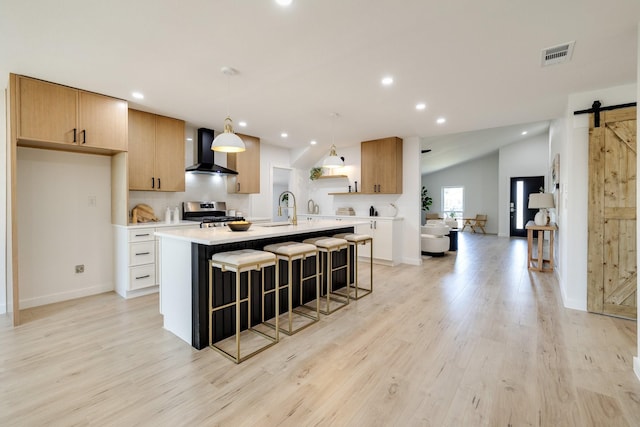 4128 Blackwillow Dr, Mesquite, TX 75150 - kitchen with wall chimney exhaust hood, a barn door, stainless steel gas stove, light countertops, and an island with sink