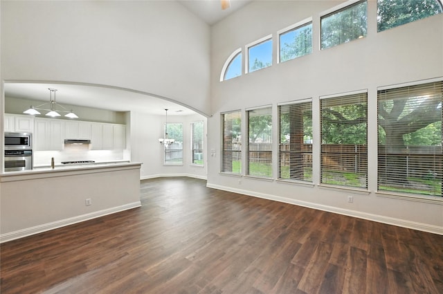 3816 Appleton Ln, Flower Mound, TX 75022 - unfurnished living room featuring dark wood-style floors, a chandelier, a towering ceiling, and arched walkways
