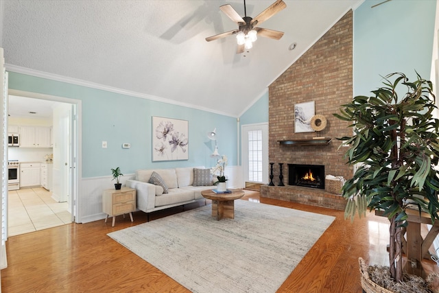 132 Cherrybark Dr, Coppell, TX 75019 - living area featuring light wood-style flooring, a fireplace, a ceiling fan, wainscoting, and high vaulted ceiling
