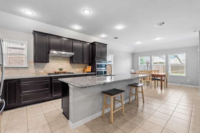 952 Sweeping Butte Dr, Fort Worth, TX 76052 - kitchen with under cabinet range hood, stainless steel appliances, light stone countertops, light tile patterned floors, and a breakfast bar