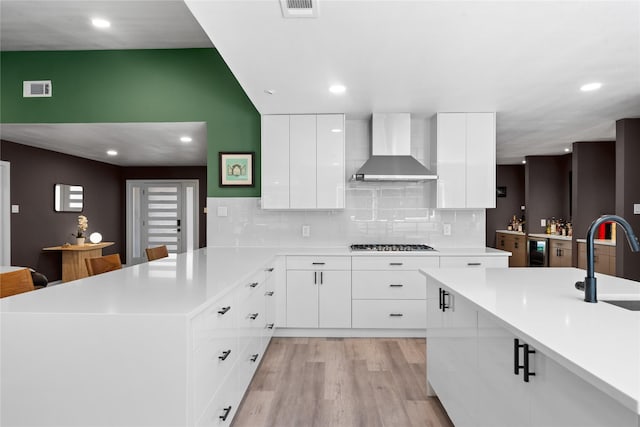 9918 Ila Dr, Dallas, TX 75220 - kitchen with wall chimney range hood, a peninsula, black stovetop, a sink, and light countertops