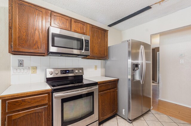 1824 Angelina Dr, Garland, TX 75040 - kitchen with appliances with stainless steel finishes, light countertops, backsplash, brown cabinetry, and a textured ceiling