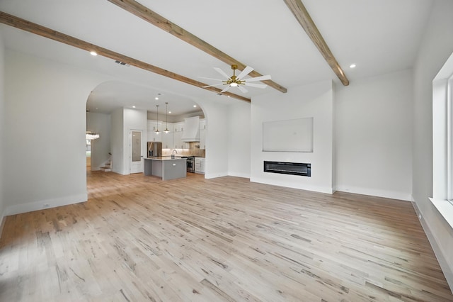 1224 S Pine St, Grapevine, TX 76051 - unfurnished living room with arched walkways, beam ceiling, ceiling fan, a glass covered fireplace, and light wood-style flooring