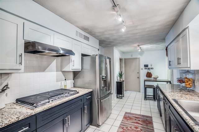10542 Vinemont St, Dallas, TX 75218 - kitchen featuring track lighting, under cabinet range hood, stainless steel appliances, light tile patterned floors, and backsplash
