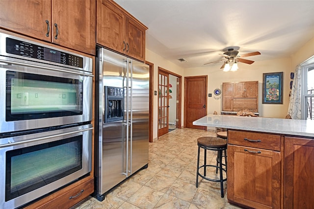 2112 Columbia Dr, Richardson, TX 75081 - kitchen featuring appliances with stainless steel finishes, light countertops, brown cabinets, a breakfast bar, and ceiling fan