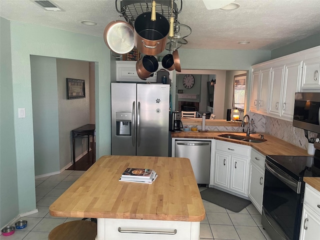 5907 Aloe Ct, Arlington, TX 76017 - kitchen featuring stainless steel appliances, wooden counters, light tile patterned floors, white cabinetry, and a textured ceiling