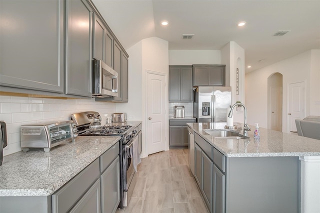 7200 Paso Verde Dr, Fort Worth, TX 76131 - kitchen featuring stainless steel appliances, a sink, gray cabinetry, arched walkways, and an island with sink