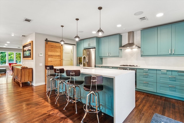 133 Lakeridge Dr, Dallas, TX 75218 - kitchen featuring wall chimney range hood, stainless steel appliances, a kitchen island with sink, dark wood-style flooring, and tasteful backsplash