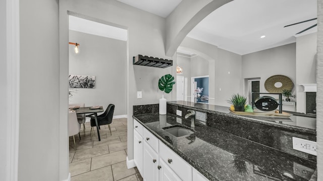 5709 Courtney Cir, Haltom City, TX 76137 - kitchen featuring a sink, dark stone countertops, white cabinetry, arched walkways, and baseboards