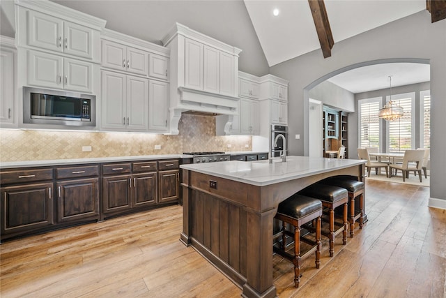 6286 Brentway Rd, Frisco, TX 75034 - kitchen with stainless steel appliances, arched walkways, light wood-type flooring, a kitchen bar, and high vaulted ceiling