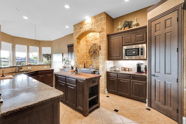 11667 Bent Creek Trl, Frisco, TX 75033 - kitchen featuring stainless steel microwave, light tile patterned flooring, wood counters, backsplash, and dark brown cabinetry