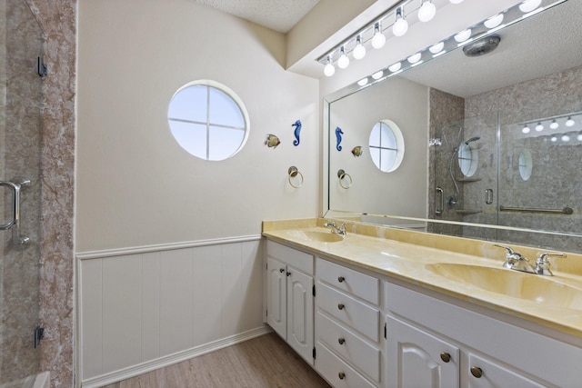 1720 Norwood Dr, Hurst, TX 76054 - bathroom with wood finished floors, double vanity, a stall shower, wainscoting, and a textured ceiling