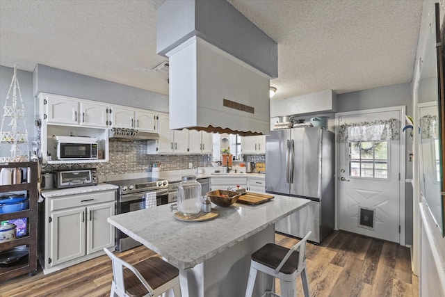 500 W San Diego St, Detroit, TX 75436 - kitchen with stainless steel appliances, a textured ceiling, under cabinet range hood, wood finished floors, and backsplash