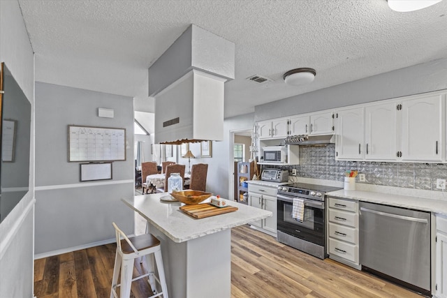 500 W San Diego St, Detroit, TX 75436 - kitchen with appliances with stainless steel finishes, white cabinets, decorative backsplash, light wood-type flooring, and a kitchen bar