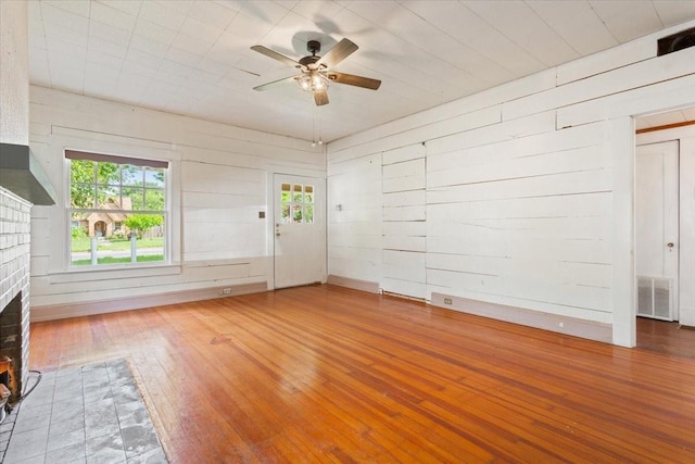 2600 Colcord Ave, Waco, TX 76707 - unfurnished living room with hardwood / wood-style floors, a fireplace, ceiling fan, healthy amount of natural light, and wood walls