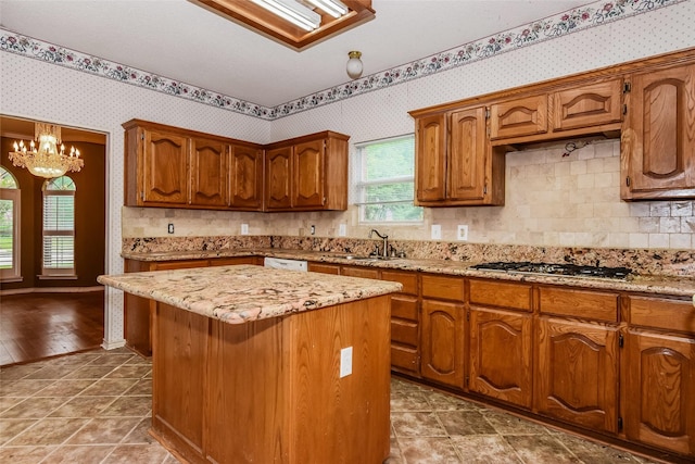 4005 Cavalier Dr, Rowlett, TX 75088 - kitchen featuring wallpapered walls, a chandelier, a kitchen island, brown cabinetry, and stainless steel gas stovetop