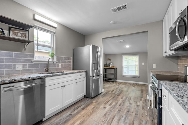 406 N Ruddell St, Denton, TX 76209 - kitchen with stainless steel appliances, a sink, light wood-type flooring, white cabinetry, and backsplash