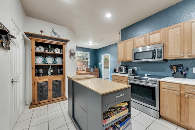 1053 Pullman Dr, Saginaw, TX 76131 - kitchen featuring stainless steel appliances, light brown cabinetry, light tile patterned floors, a center island, and a textured wall