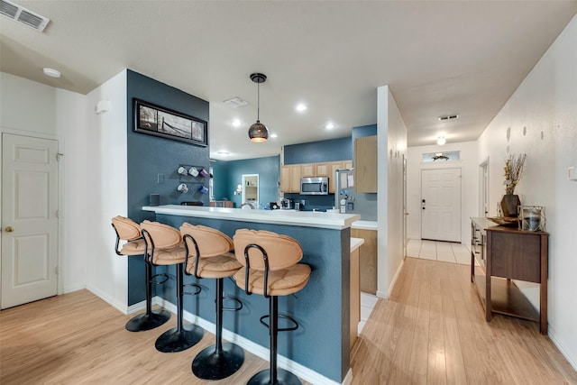 1053 Pullman Dr, Saginaw, TX 76131 - kitchen featuring stainless steel microwave, light wood-style floors, a peninsula, a breakfast bar area, and recessed lighting