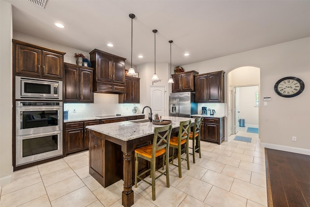 217 Golden Arrow Dr, Weatherford, TX 76087 - kitchen featuring stainless steel appliances, a sink, dark brown cabinetry, tasteful backsplash, and a breakfast bar area