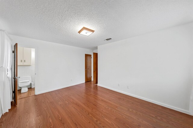 120 Wooded Crest Dr, Woodway, TX 76712 - unfurnished bedroom featuring wood finished floors, a textured ceiling, baseboards, and connected bathroom
