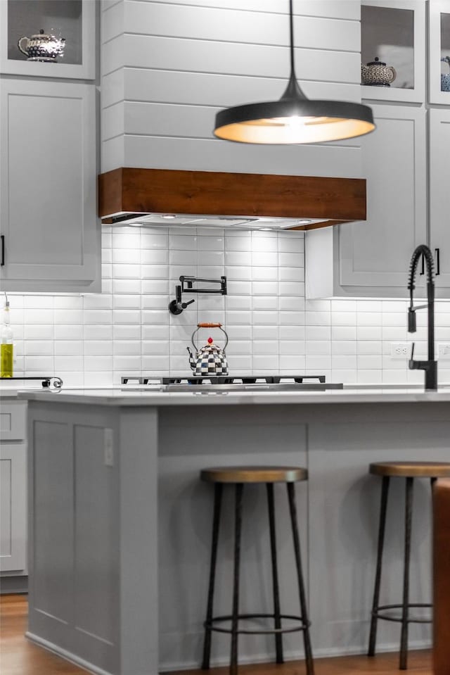 1907 Cedar Bluff Pkwy, Mansfield, TX 76063 - kitchen with a breakfast bar, backsplash, glass insert cabinets, gray cabinetry, and stainless steel gas cooktop