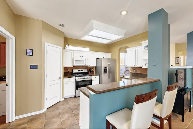 4533 Crooked Ridge Dr, The Colony, TX 75056 - kitchen with appliances with stainless steel finishes, a kitchen bar, a peninsula, dark countertops, and white cabinetry